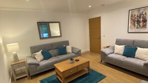 A modern living room with two grey sofas, a wooden coffee table, a teal rug, and a small side table with a lamp.