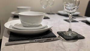 A dining table with a white bowl and a wine glass on a marble surface, with a framed picture of fruit on the wall behind.