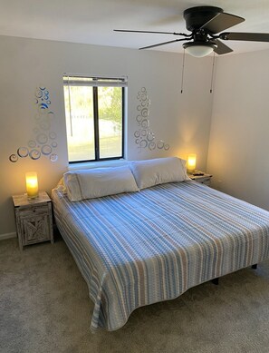 A bedroom with a bed, a ceiling fan, a window, and two bedside lamps.