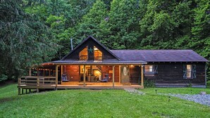A rustic cabin with a porch, a central chimney, and a deck.