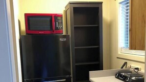 Eine kleine Küche mit einem schwarzen Kühlschrank, einer Mikrowelle und einem Holzschrank.