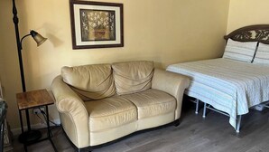 Ein Zimmer mit beiger Ledersofa, Nachttisch, Lampe und einem Bett mit gestreifter Bettdecke.