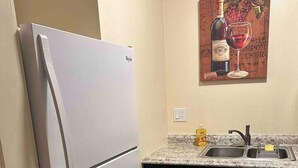 Una cocina compacta con un refrigerador blanco, encimera de granito, un lavamanos y armarios negros.