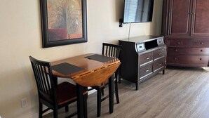 Un comedor con una mesa y sillas de madera, un televisor montado en la pared y un mueble de madera oscuro.