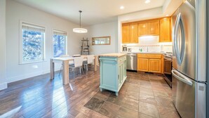 A modern kitchen with wooden cabinets, a stainless steel refrigerator, and a dining area with a table and chairs.