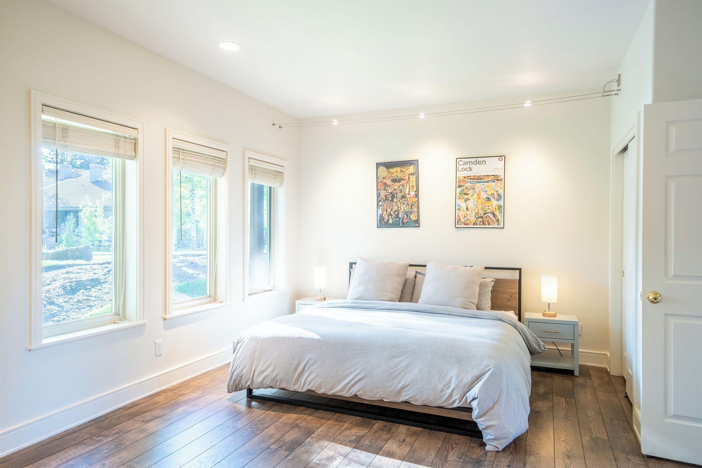 A bedroom with a large bed, two bedside tables, and two windows with blinds.