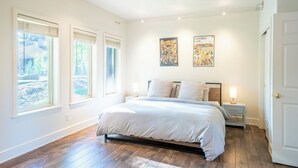 A bedroom with a large bed, two bedside tables, and two windows with blinds.