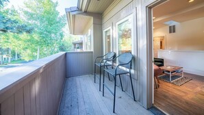 A covered outdoor area with a wooden deck, two metal chairs, and a small table with a rug.