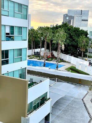 A modern building with a rooftop pool area, surrounded by palm trees and a city skyline in the background.