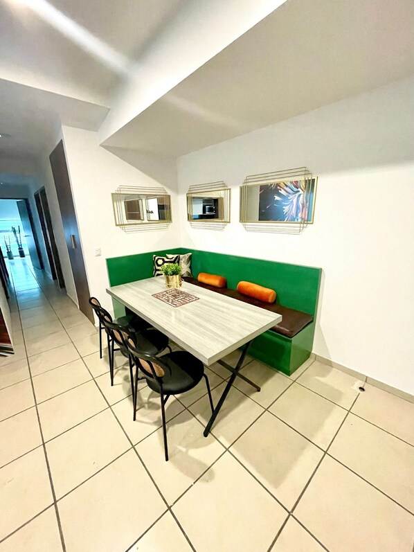 A dining area with a table and chairs, a green cushioned bench, and three framed pictures on the wall.