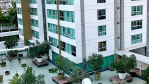 Um edifício moderno com vários andares, com amplas janelas e um pátio com plantas em vasos.