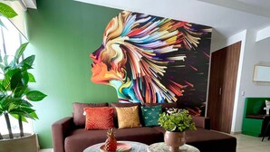 Uma sala de estar com parede verde, uma grande pintura abstrata, um sofá marrom, duas mesas redondas e um banquinho verde.
