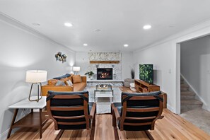A modern living room with a fireplace, wooden flooring, a sofa, two armchairs, a coffee table, and a lamp.