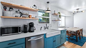 Una cocina moderna con microondas, cafetera y utensilios sobre la encimera. Se aprecia una ventana con vistas al exterior.