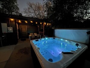Un bain à remous équipé de lumières LED, un espace patio avec des chaises et un écran de projection.