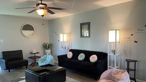 Ein Wohnzimmer mit schwarzem Sofa, Couchtisch, Sitzsack, Deckenventilator und Wanddekorationen.