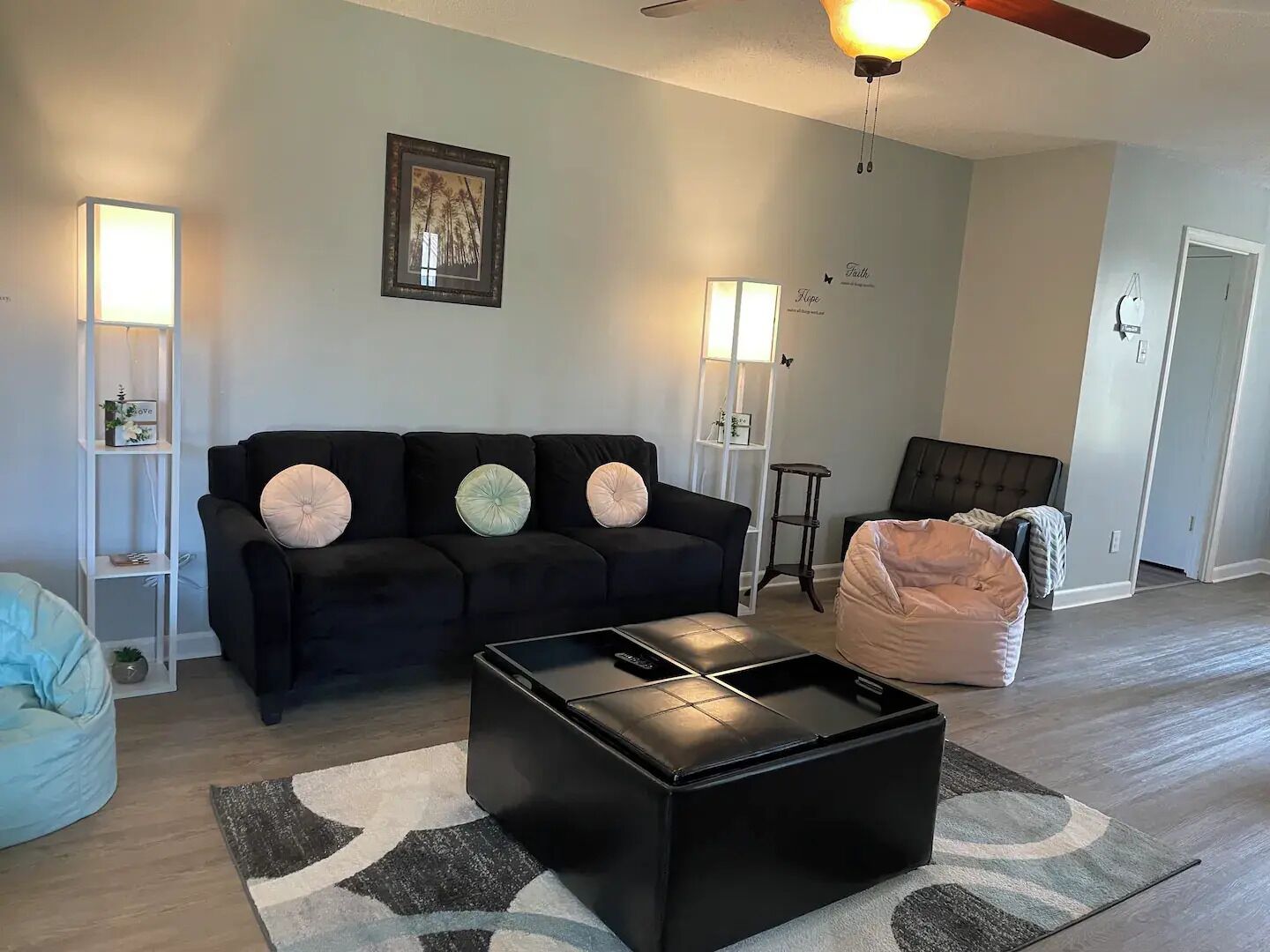 A living room with a black sofa, a black coffee table, a blue bean bag, and a grey patterned rug.