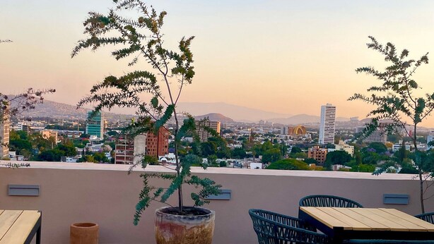 A rooftop terrace with a view of a cityscape, featuring a large potted plant, outdoor seating with chairs and tables, and a tiled floor. - Depto in beautiful Soho Morelos, new, 2 bedrooms (Guadalajara)