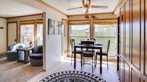 A dining area with a wooden table and chairs, a ceiling fan, and large windows with curtains. - Hiking & Explore: Brian Head Condo w/ Indoor Pool! (Brian Head)