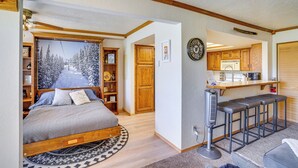 A bedroom with a bed, a nightstand, a wall clock, and a view of a kitchen area. - Hiking & Explore: Brian Head Condo w/ Indoor Pool! (Brian Head)