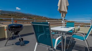 Eine Terrasse mit Grill, Stühlen und Tisch unter einem weißen Sonnenschirm.