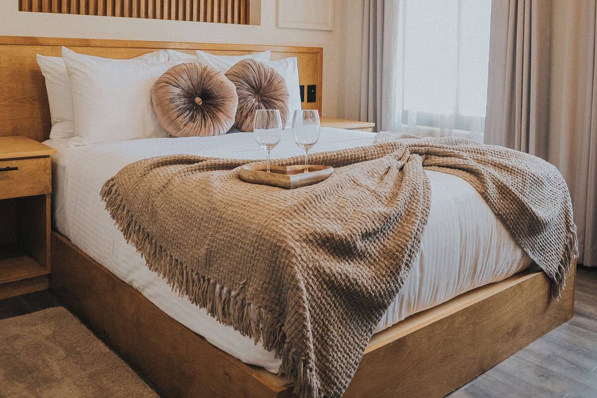 A neatly made bed with a wooden headboard, a bedside table, and a window with curtains.