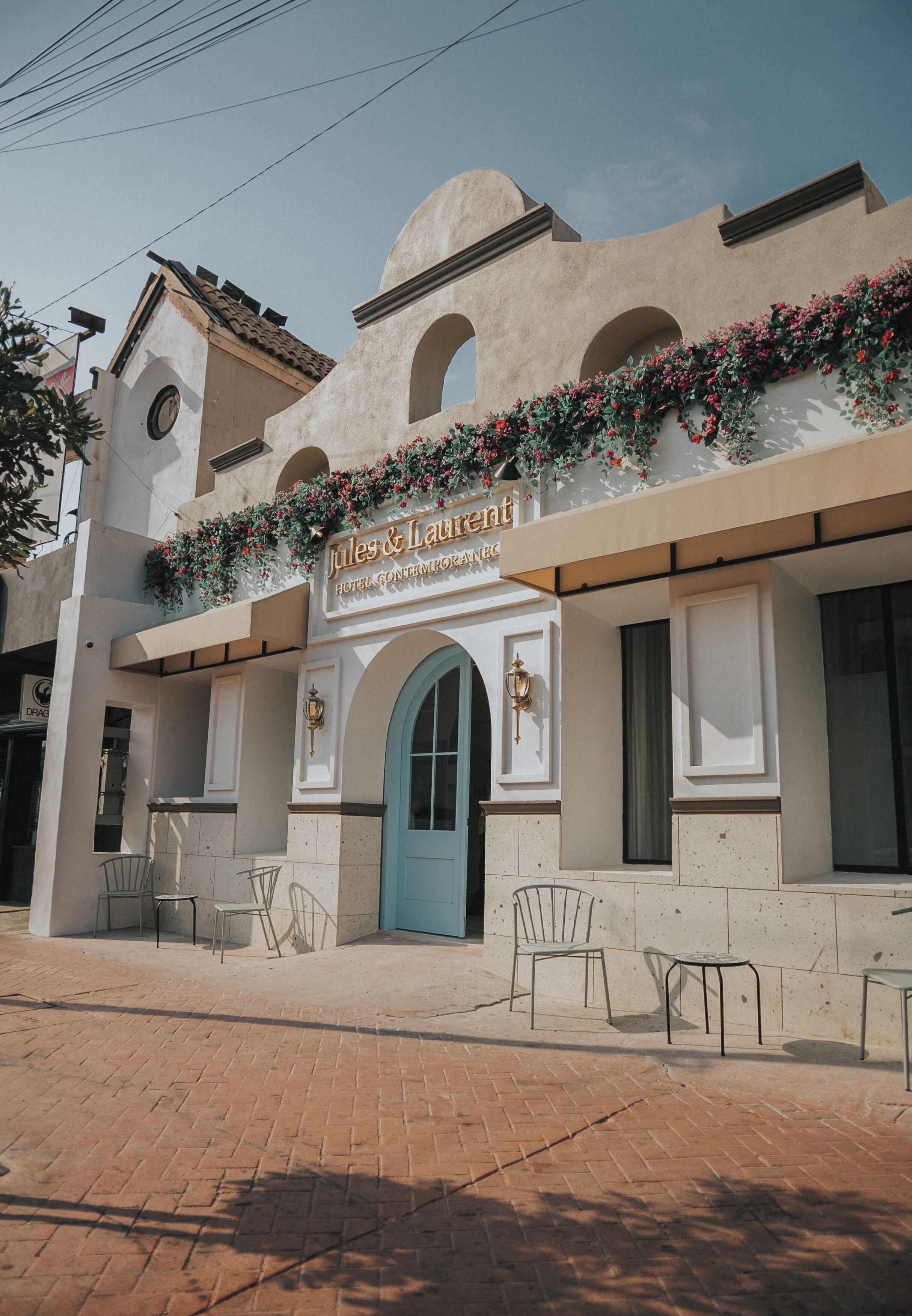 A hotel named "Jules & Laurent" with a blue door, outdoor seating area, and a flower-adorned facade.