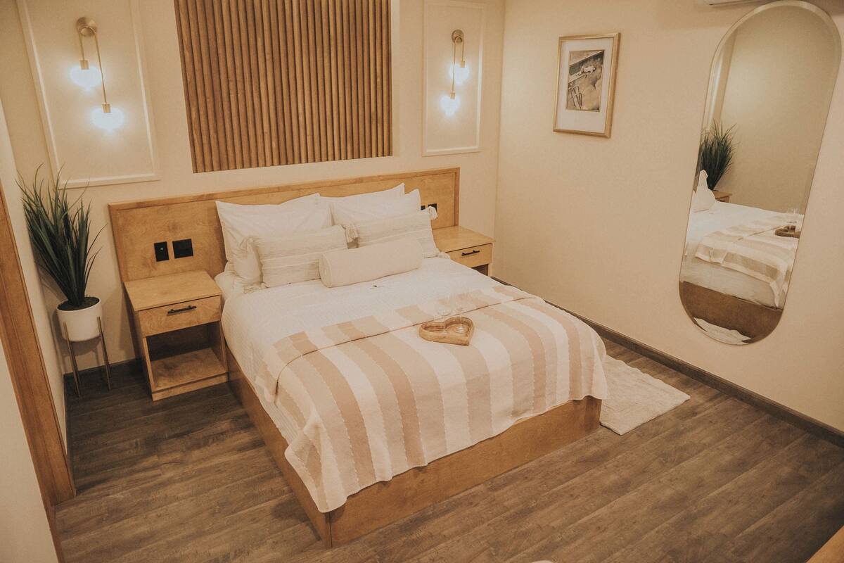 A neatly arranged bedroom with a wooden bed, bedside tables, a mirror, and wall-mounted lights.