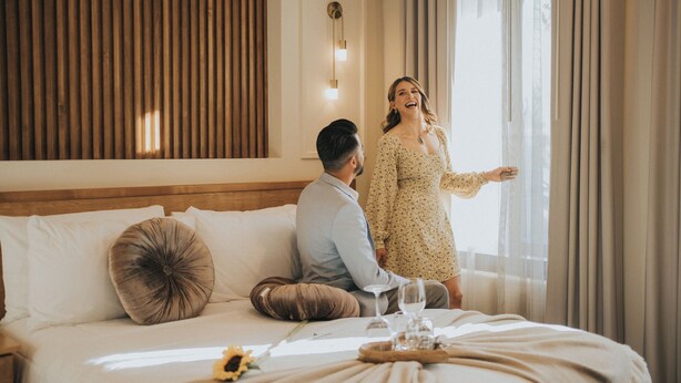 A bedroom with a bed, pillows, a bedside table with a glass of water, and a window with curtains. - Jules and Laurent Hotel Contemporaneo (Ensenada)