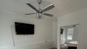 Une chambre avec un grand lit, un ventilateur de plafond, un téléviseur à écran plat et un miroir.