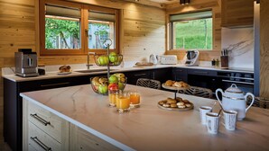 A modern kitchen with wooden beams, a large island with breakfast items, and large windows. - Chalet Anselme - luxury stay for 10 with Mont Blanc views - OVO Network (Cordon)
