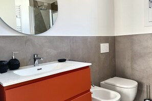 Ein modernes Badezimmer mit einem weißen Waschbecken, orangefarbenen Schränken, einem runden Spiegel und einer weißen Toilette.