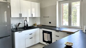 A modern kitchen with white cabinets, a stainless steel refrigerator, a black countertop, and a window with a view of greenery. - SE104 - Senigallia, elegant four-room apartment convenient to services (Senigallia)