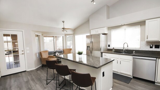 A modern kitchen with a central island, bar stools, a refrigerator, and a dishwasher.