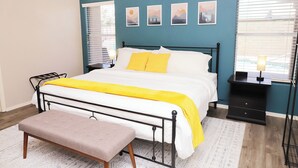 A bedroom with a bed, a bench, a nightstand, and wall art.