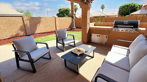 An outdoor patio with a grill, two chairs, a table, and a glass of drink.
