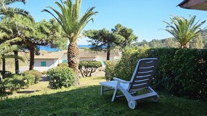 A garden with a chair, palm trees, and a building with a tiled roof.