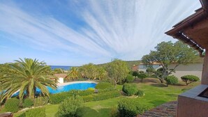 A view of a swimming pool surrounded by well-maintained greenery and a clear sky.