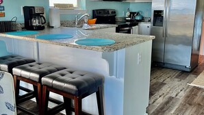 A modern kitchen with white cabinets, a stainless steel refrigerator, a built-in microwave, and a coffee maker. - Stunning balcony sunsets, 2 minute walk to beach, lil piece of heaven! (Navarre)
