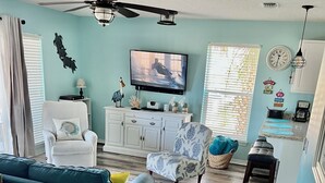 A living room with a blue sofa, a white armchair, a television, and a ceiling fan. - Stunning balcony sunsets, 2 minute walk to beach, lil piece of heaven! (Navarre)