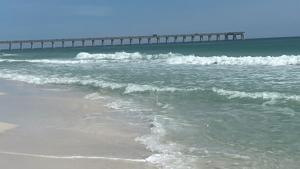 A beach with waves and a pier in the background. - Stunning balcony sunsets, 2 minute walk to beach, lil piece of heaven! (Navarre)