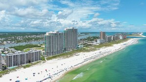 A coastal cityscape with a beachfront hotel, a sandy beach, and a clear blue sky. - The Palms 804 - RELAX AT THE  BEACH IN THIS GORGEOUS GULF FRONT CONDO! (Orange Beach)