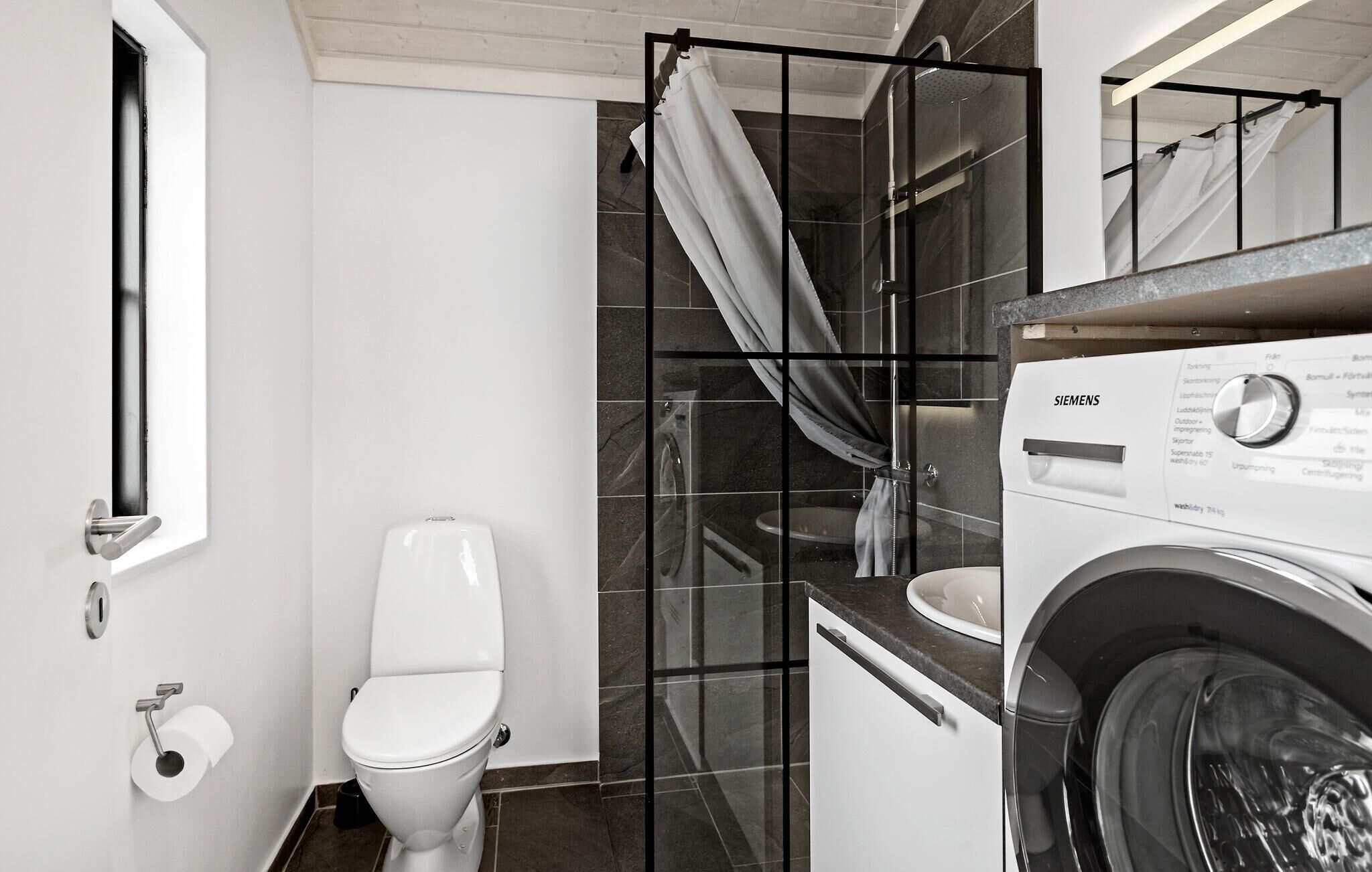 A compact bathroom with a toilet, a shower with a glass door, and a washing machine.