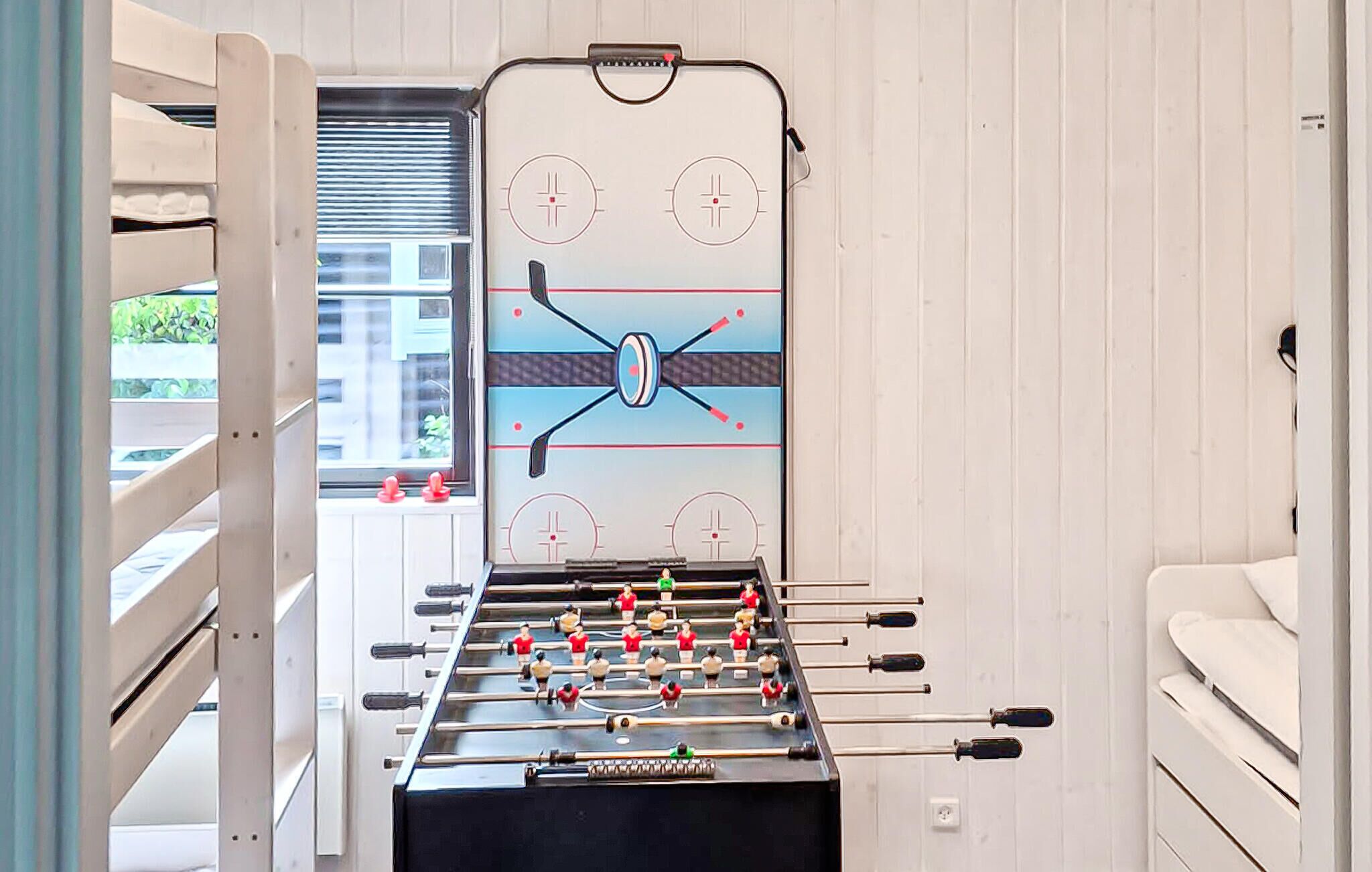 Une table de baby-foot dans une pièce avec une fenêtre, un lit et un mur blanc.