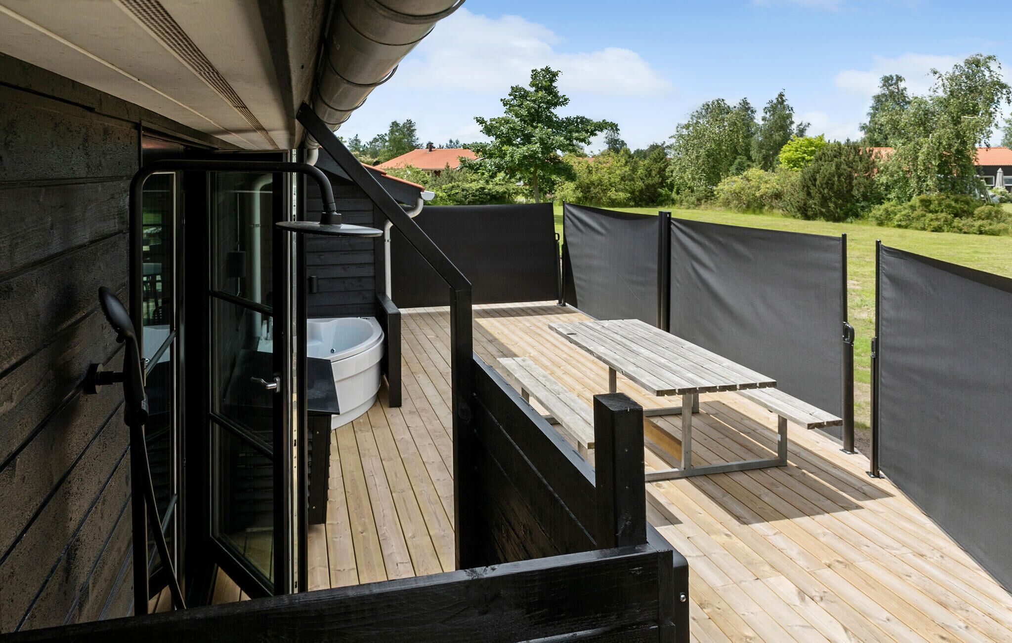A wooden deck with a hot tub and a table, surrounded by a black fence.