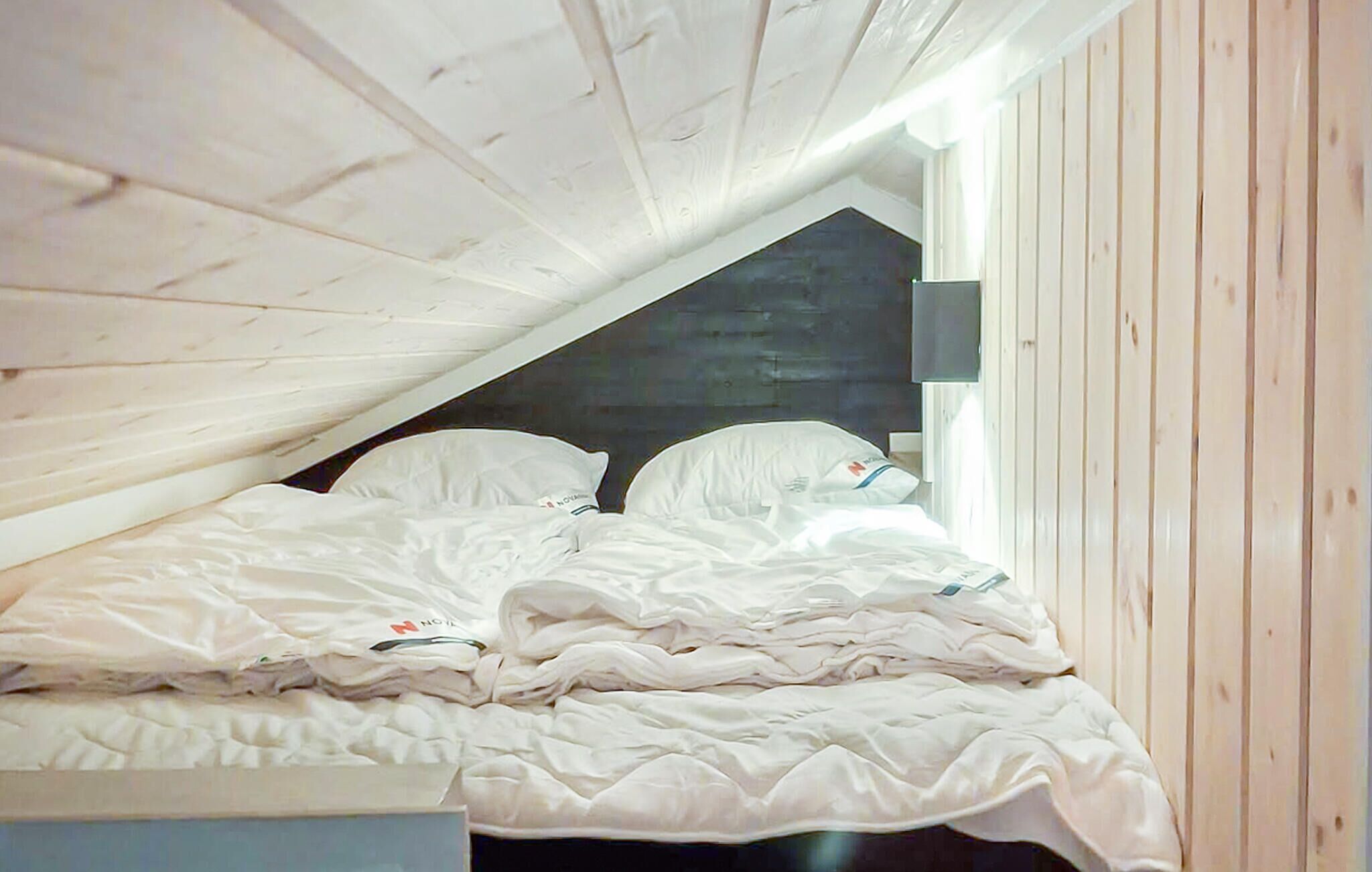 Una habitación con techo inclinado, paredes de madera, una cama con ropa de cama blanca y una ventana con vistas al exterior.