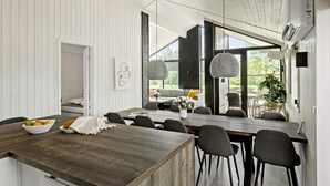 Una cuina moderna amb taulell de fusta, zona de menjador amb taula gran i cadires, i vistes a l'exterior.