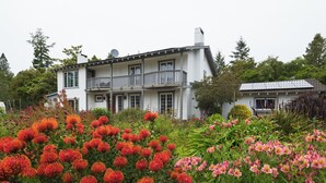 Una casa a due piani con un balcone, immersa in un giardino fiorito di fiori rossi e rosa.