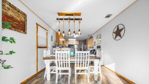 A dining area with a wooden table and white chairs, a kitchen in the background, and a star decoration on the wall. - Randy's Place - Beautiful 4br W/Private Hot tub! (Bandera)