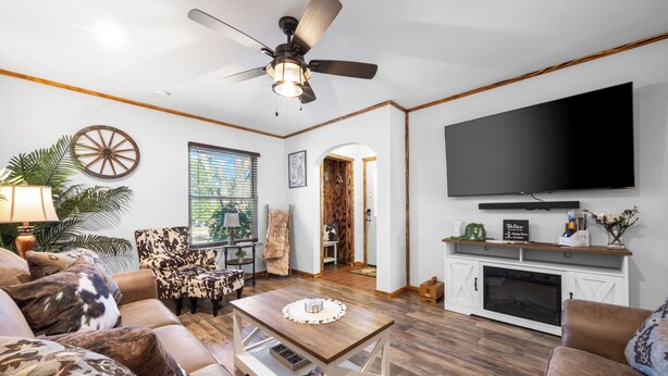 A living room with a large flat-screen TV, a ceiling fan, a wooden coffee table, and a fireplace. - Randy's Place - Beautiful 4br W/Private Hot tub! (Bandera)